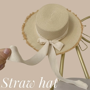 Detail of a beige flat-top straw hat with elegant long ribbon bow on a golden chair