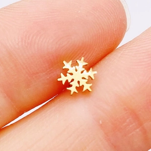 Macro shot of gold snowflake stud earring held between fingers for size reference