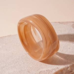 Detail of amber acrylic wide band ring with marble texture on a natural stone base