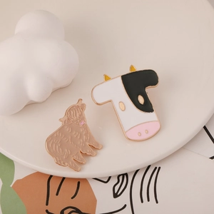 Detailed view of cute enamel animal pins featuring a cow and alpaca on a ceramic plate