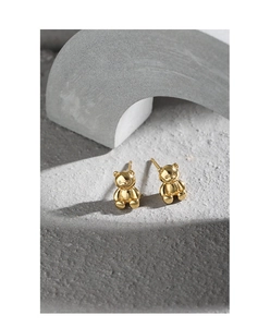 Macro detail of golden bear stud earrings on a textured minimalist display