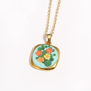 Close-up of golden square pendant with enamel floral pattern and blue eye detail