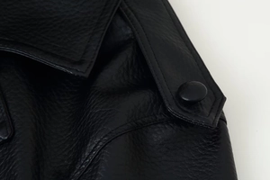 Detail of shoulder epaulette with button on black faux leather biker jacket