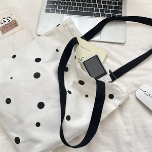 Close-up of a large capacity polka dot canvas tote bag with black woven handles and laptop