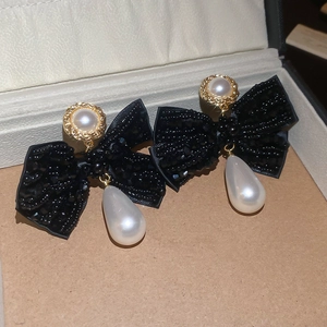 Macro shot of bow earrings with black beads and dangling white drop pearls in a box