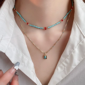 Close-up of bohemian layered necklace with turquoise beads and gold square pendant