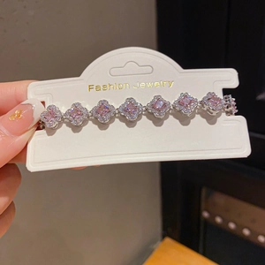 Detail of silver clover bracelet with pink zircon stones on a white jewelry display card