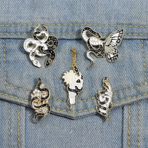 Enamel snake and butterfly pins displayed on a denim jacket pocket in dark gothic style