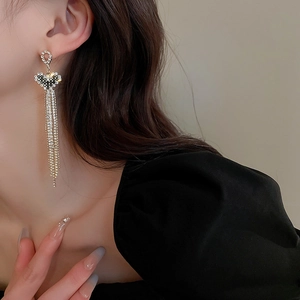 Close-up of heart-shaped gold tassel earrings with sparkling crystals worn by a model