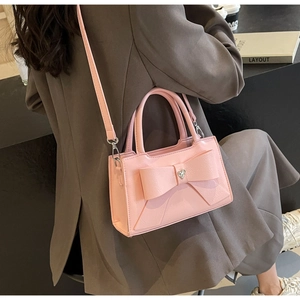 Pink bow handbag with heart-shaped rhinestone detail worn by model in a cafe setting
