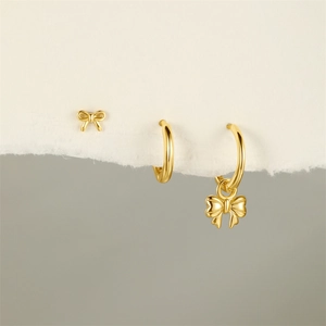 Detailed view of gold bow earrings and hoop set displayed on minimalist white torn paper