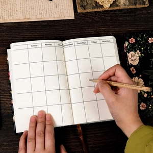 Top-down view of a vintage black floral notebook showing monthly plan layout and white pages