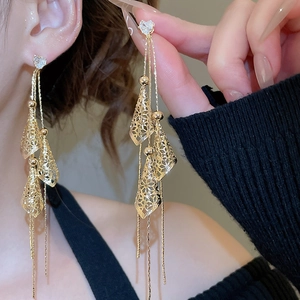 Detailed view of long gold tassel earrings with heart studs and hollow cone charms on model