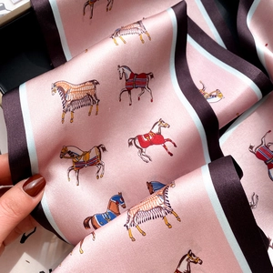 Pink silk scarf with horse patterns and blue-brown borders, held to show smooth texture