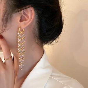 Close-up of elegant gold tassel earrings with pearls on a model showing draping style