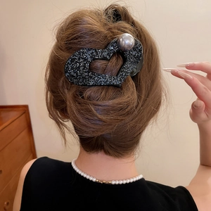 Detail showing a large black heart-shaped hair claw clip with rhinestones and a large pearl