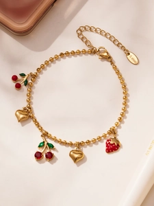 Détail d'un bracelet en perles dorées avec des breloques cerise, fraise et cœur