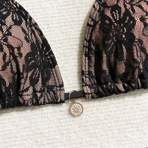 Macro detail of black floral lace bikini top with a sun-engraved golden metal pendant