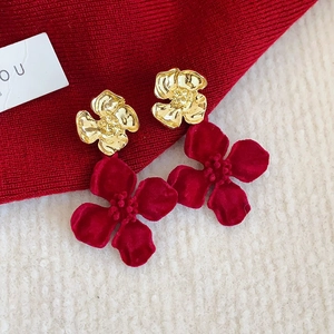 Detail of red flocked flower earrings with golden metal stamen on textured fabric