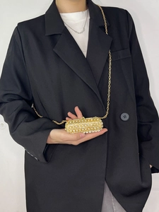 Close-up of golden rhinestone lipstick bag with metal chain strap held by a model