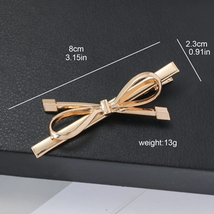 Metallic gold bow hair clip measuring 8cm by 2.3cm on a black leather background