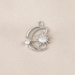 Macro view of a silver moon and sun pendant with zircon crystals on silk fabric