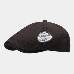 Detail of a dark brown cotton beret featuring a side-stitched shield logo patch