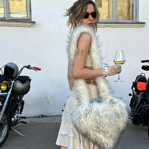 Outdoor view of a large white heart-shaped faux fur crossbody bag worn by a model