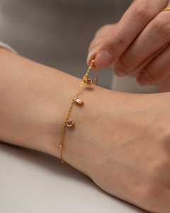 Gros plan d'un bracelet en titane doré avec des pendentifs en pierres précieuses mauves