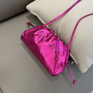 Close-up of metallic rose red dumpling bag with pleated texture on a soft beige pillow