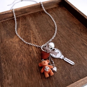 Detailed close-up of flocked bear, plaid bow, and Lucky key charms on a long chain necklace