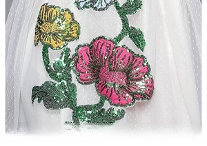 Détail de broderie florale en paillettes colorées sur tissu en maille à pois blancs