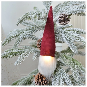 Close-up of a glowing red knitted Christmas gnome hanging on a snowy tree branch