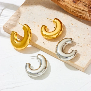 Detail of C-shaped gold and silver chunky hoop earrings on textured stone surface