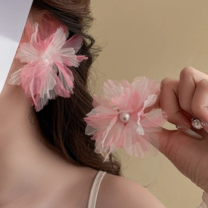 Close-up of pink tulle flower earrings with pearl accent worn by a model in soft light