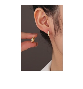 Detailed close-up of a twisted gold hoop earring with pavé zircon stones worn on the ear