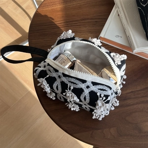 Detail of black canvas bag featuring white embroidery with tassels and cosmetic items