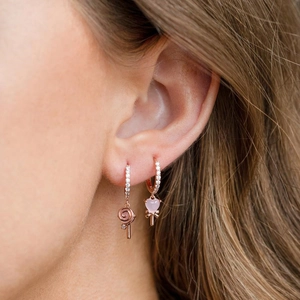 Close-up of rose gold lollipop and pink heart earrings with zircons on model ear