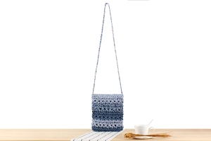 Detail of blue and white gradient hand-woven crossbody bag on a bright wooden table