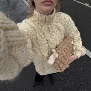 Off-white cable knit turtleneck sweater paired with a textured brown knit clutch bag