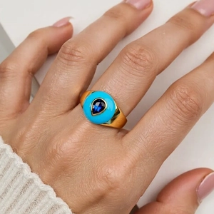 Close-up of a gold ring with a turquoise round stone and pear-cut deep blue center gem