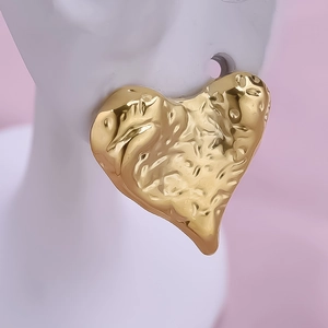 Detail view of large 18k gold heart-shaped earrings with unique hammered texture on model