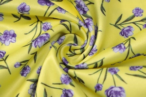 Close-up of yellow floral fabric showing purple flower patterns and silky texture