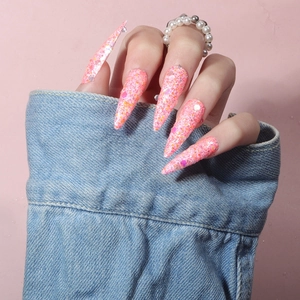 Close-up of long stiletto press-on nails with iridescent pink and orange glitter sequins