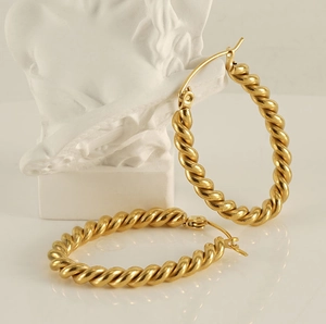 Close-up of golden oval twisted earrings on white marble, elegant vintage style design