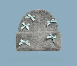Dettaglio del berretto in maglia grigio chiaro con cinque fiocchi di raso azzurro