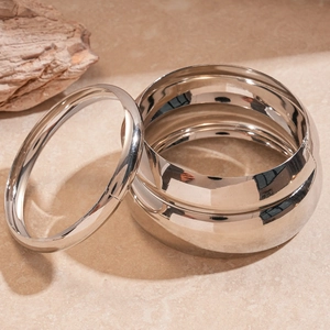 Polished silver-tone geometric metal bangles set on a minimalist marble surface