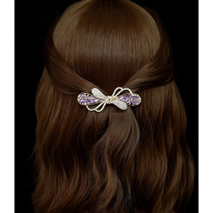 Elegant gold bow hair clip with purple crystal embellishments worn by a model