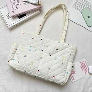 Close-up of cream quilted tote bag with heart embroidery and multiple outer pockets