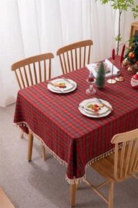 Detail of red and black plaid Christmas tablecloth featuring white fringe on wooden table